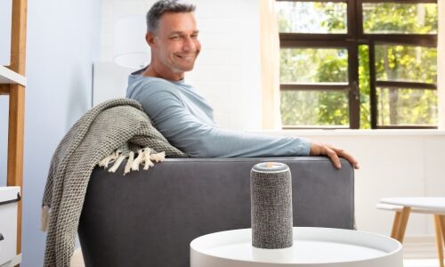Man in baby boomer demographic sitting on sofa and listening to wireless smart speaker. Smart home technology